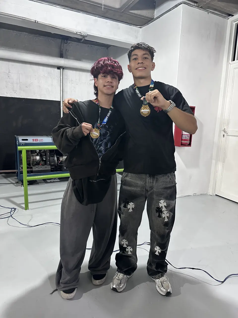 Dos atletas mostrando su medalla de la competencia a la cámara.